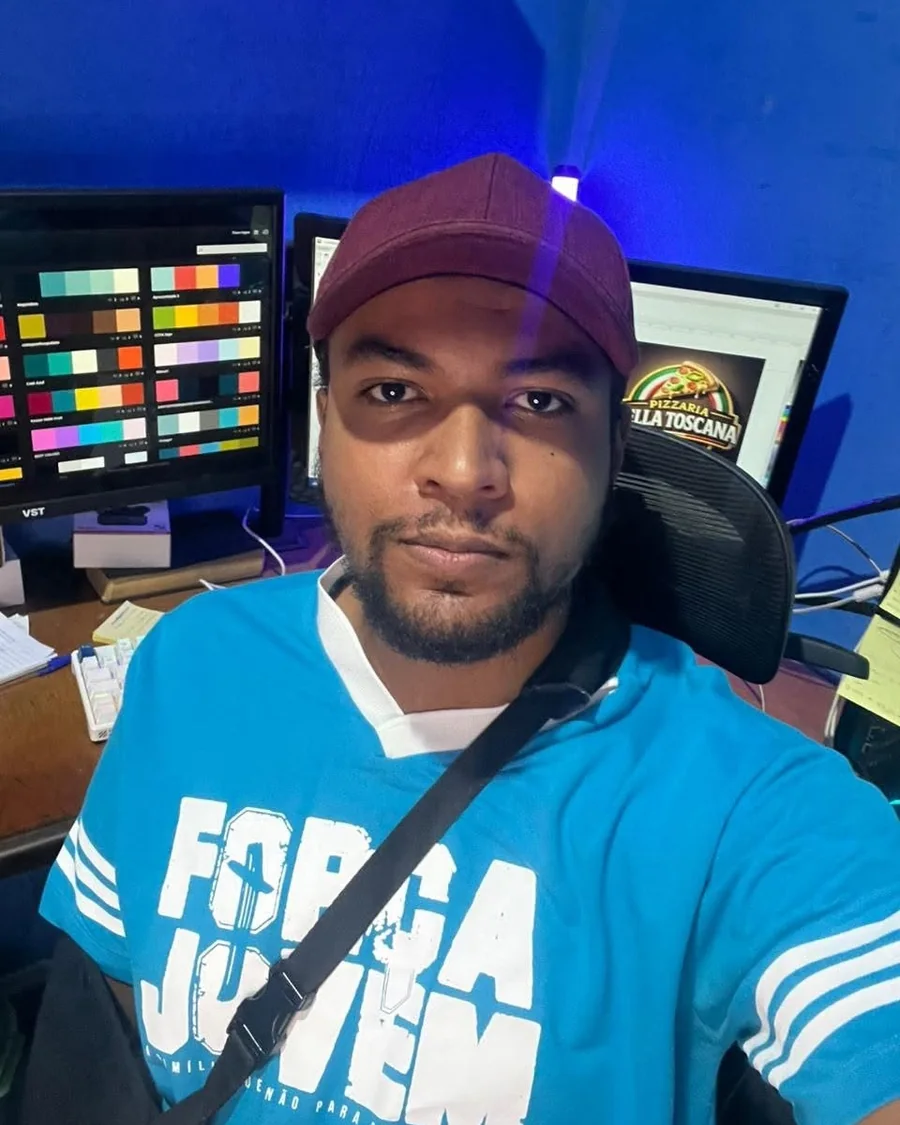 Dion Soares, designer e fundador da Dion Logos, no estúdio em Palmas com paletas de cores e uma logo de pizzaria nos monitores